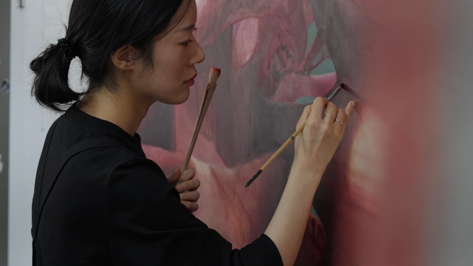 임지현 작가 필름의 한 장면. 작가가 붓 두 자루를 쥐고 붉은 화면 앞에 서 있다.