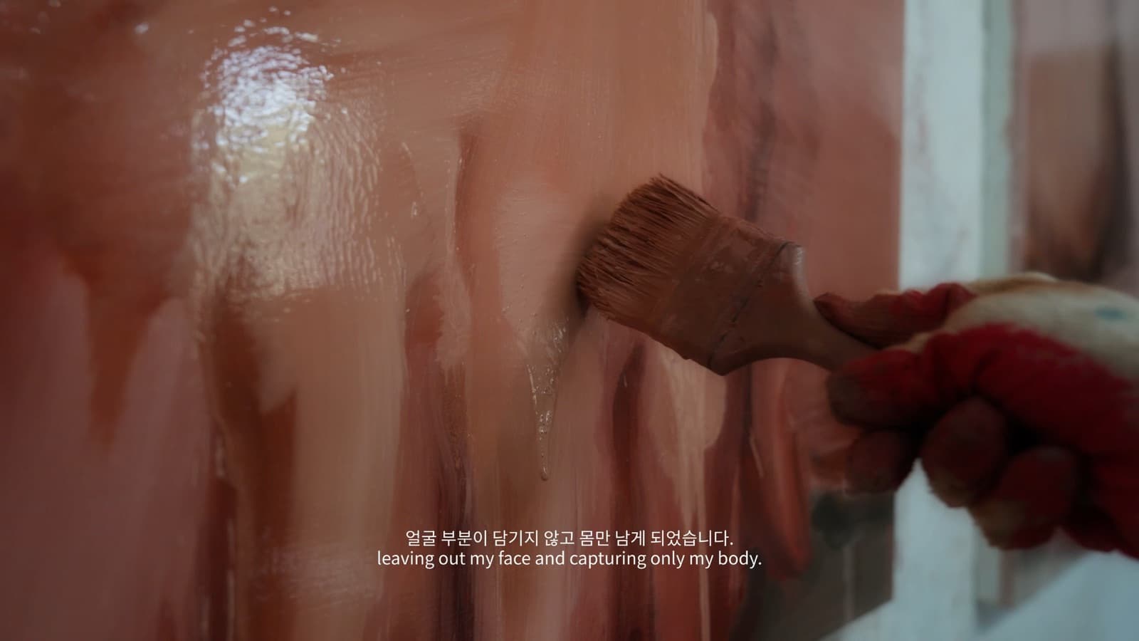 김찬송 작가 필름의 한 장면. 붉은 장갑을 낀 손이 넓은 붓으로 살색 화면을 쓸어내린다.
